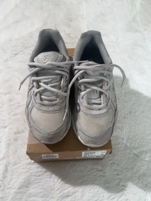 Gråa Asics sneakers i mesh och mocka - Snygga gråa sneakers från Asics med ovandel i mesh och detaljer i mocka. Skorna har klassisk snörning, låg profil och en chunky sula som ger en sportig vibe. Perfekta för dig som gillar stilrena och bekväma sneakers.