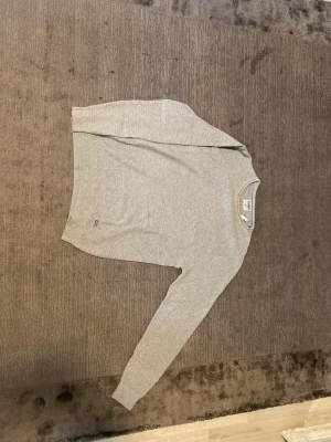 Ljusgrå strukturerad tröja SAMS - Ljusgrå långärmad tröja från SAMS med snyggt rutmönster i tyget. Tröjan har rund halsringning och är gjord i ett mjukt material som känns skönt mot huden. Perfekt för dig som gillar en clean och stilren vibe.