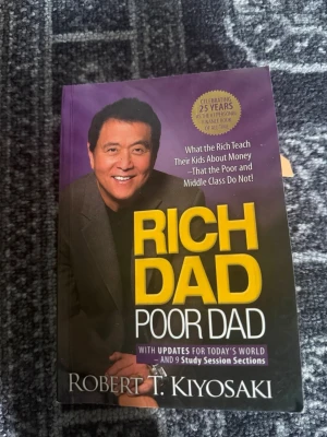 Rich Dad Poor Dad av Robert Kiyosaki - En populär bok med lila och gul framsida, skriven av Robert T. Kiyosaki. 'Rich Dad Poor Dad' handlar om ekonomi, pengar och hur man tänker kring investeringar. Perfekt för dig som vill lära dig mer om privatekonomi och entreprenörskap.