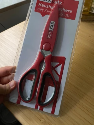 Röda hushållssaxar från XXXLutz - Säljer ett par röda hushållssaxar från XXXLutz med svarta detaljer och ergonomiska handtag. Saxarna är tillverkade i metall och plast och levereras i originalförpackning. Perfekta för köket eller pyssel.