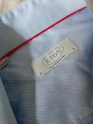 Ljusblå skjorta från Eton - Säljer en klassisk ljusblå skjorta från Eton i modellen Contemporary. Skjortan har lång ärm, vita knappar och en snygg röd detalj på insidan av kragen. Perfekt för dig som gillar stilrena plagg med bra passform.