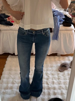 Blå bootcut jeans med låg midja, replay - Snygga blå bootcut jeans med låg midja och klassiska fem fickor. Jeansen har en lätt tvättad look och utsvängda ben, perfekta för en trendig och avslappnad stil. Passar dig som gillar en retro vibe och vill ha ett par jeans som sticker ut.