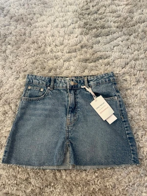 Jeanskjol - Trendig blå jeanskjol från Gina Tricot. Kjolen har bälteshällor, knapp- och dragkedjestängning samt en rak, kort passform. Perfekt att matcha med en t-shirt eller hoodie. Aldrig använd och prislappen sitter kvar