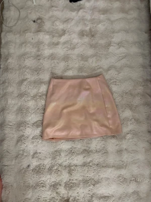 Glittrig rosa minikjol - Superfin kort kjol i glittrigt rosa material med lätt skimrande yta. Kjolen har en enkel, rak passform och är perfekt för att sticka ut lite extra. Passar dig som gillar trendiga och lekfulla plagg.
