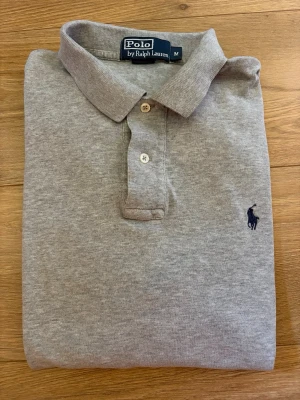 Polo Ralph Lauren Piké - En klassisk snygg grå piké från Polo Ralph Laurent. Storlek M sitter perfekt. Inga defekter alls, använda några gånger. Skick 9/10. Pris kan diskuteras vid snabb affär!
