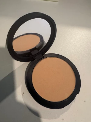  puder i beige nyans,  - Ett  puder i en rund svart dosa med spegel. Pudret har en ljusbeige ton och är i kompakt form, perfekt för att matta ner huden och ge en jämn finish. Materialet är klassiskt puder och dosan är smidig att ta med i väskan. Jag älskar deras produkter, de har ett väldigt bra märke, med bra kvalité, mitt smink håller jättebra, jag har deras setting spray och cc cream älskarrr! Mina vänner frågade mig mycket om varför mitt smink sitter så bra. Rekommenderar, vad väntar du på, låt din smink sitta fint 