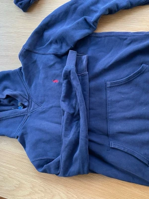 Mörkblå hoodie från Polo Ralph Lauren - Snygg mörkblå hoodie från Polo Ralph Lauren med klassisk huva och stor känguruficka framtill. Broderad röd logga på bröstet. Mjuk bomullsmix som är skön att ha på sig. Perfekt för en chill och stilren look.