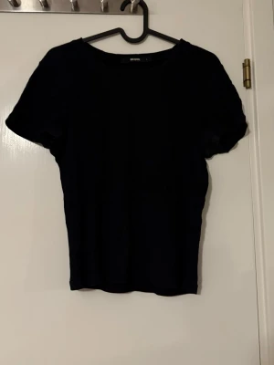Svart ribbad t-shirt från BikBok - En svart ribbad t-shirt från BikBok i storlek L. T-shirten har rund halsringning och korta ärmar, perfekt för en clean och enkel stil. Materialet är stretchigt och sitter snyggt på kroppen. Passar till allt och är lätt att matcha med andra plagg.