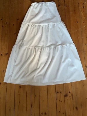 Vit långkjol från Gina Tricot - Säljer en vit långkjol från Gina Tricot med volangdetaljer. Kjolen har en luftig och flowy passform, perfekt för varma dagar. Tillverkad i ett mjukt och tunt tyg som känns skönt mot huden. Använt mycket förr💖
