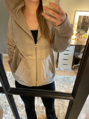 Beige ziphoodie med huva - Snygg beige hoodie med dragkedja och huva. Modellen har två stora fickor framtill och ribbade muddar vid ärmslut och nederkant. Perfekt för en avslappnad och stilren look. Tillverkad i mjukt och bekvämt material. Ej använt alls mycket, dinns nått lärke/fläck ca halv cm på ena ärmen. Ej bra pris,, skriv