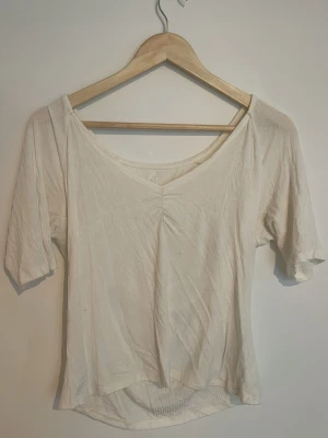 Vit ribbad topp med v-ringning - En enkel och stilren vit topp med v-ringad hals och ribbad struktur. Toppen har korta ärmar och lösare passform. Perfekt att matcha med jeans eller kjol för en clean look❣️