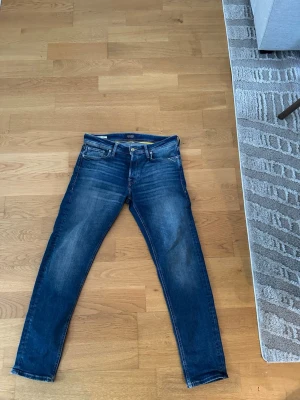 Blå slim fit jeans från Jack & Jones - Säljer ett par blå slim fit jeans från Jack & Jones med klassisk femficksmodell och snygga slitningar på låren. Jeansen har normal midja, dragkedjegylf och är tillverkade i denim med lätt stretch för extra komfort.