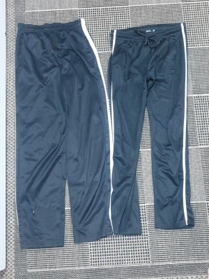 Bådar för 120kr Svarta mjukisbyxor med vita ränder - Två par svarta mjukisbyxor från Active med vita ränder längs sidorna. Byxorna har resår i midjan och är gjorda i 100% polyester för en sportig och bekväm känsla. Perfekta för chill eller träning. Säljes tillsammans!