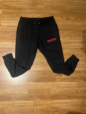Svarta mjukisbyxor från Hoodrich - Svarta mjukisbyxor från Hoodrich med röd logga på vänster lår. Byxorna har dragsko i midjan, muddar vid bensluten och två sidofickor. Perfekta för chill outfit. Ny pris på dessa byxor ligger runt 900!!!! Hos mig bara 449kr. 