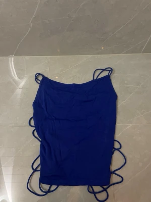 Blå linnetopp med snörning - Trendig blå linnetopp med tunna axelband och långa snören på sidorna som kan knytas på olika sätt. Toppen är ärmlös och har en tight passform.