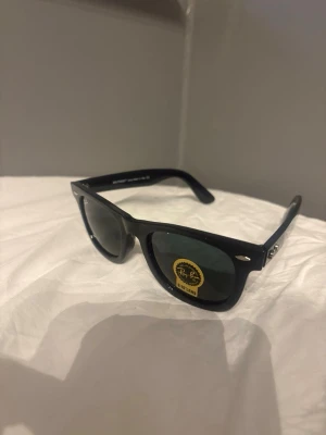 Ray-Ban Wayfarer glasögon svarta - Säljer ett par helt nya och oanvända Ray-Ban Wayfarer (RB2140-F) i klassisk svart färg.  • Modell: RB2140-F 1278/3F • Storlek: 50□22 147 • Hand Made in Italy • 100% UV-skydd  Inga repor, inga märken – aldrig använda. Klassisk och tidlös modell som alltid är trendig.  Säljes då de inte kommit till användning.