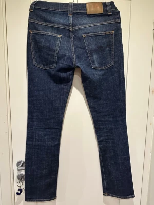 Mörkblå raka jeans med kontrastsömmar - Snygga mörkblå jeans med raka ben och klassiska kontrastsömmar. Jeansen har fem fickor, bälteshällor och en läderpatch bak i midjan. Perfekta för en avslappnad och stilren look. Tillverkade i slitstark denim.