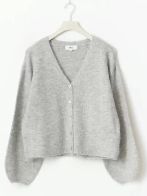 Ljusgrå stickad kofta Gina - Mysig ljusgrå stickad kofta med v-ringning och knappar framtill. Koftan har ballongärmar och en avslappnad passform. Perfekt att slänga över en t-shirt eller topp för en chill look.