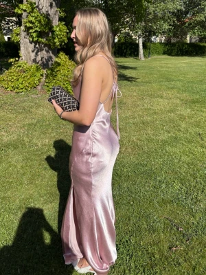 Balklänning  - Säljer min ljusrosa/ puderrosa balklänning i satin som är köpt på Nelly men från märket True Decadence! Jag är 165 lång och på bilderna har jag normal höga klackar så den släpar lite i marken, men klänningen har inga synliga defekter av det. Snörena i ryggen är justerbara och kan knytas hur man vill. Den har en fin slips på vänster ben. Klänningen är använd 2 gånger men fortfarande superfint skick!💗
