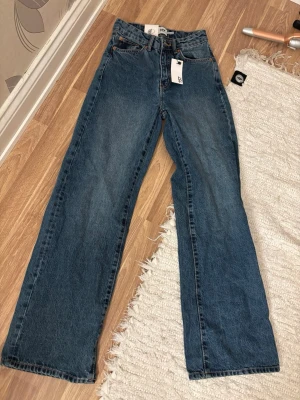 Blå raka jeans från Lee - Säljer ett par klassiska blå jeans från Lee med rak passform och hög midja. Jeansen har fem fickor, bälteshällor och stängs med knapp och dragkedja. Perfekta för en avslappnad och trendig stil.