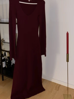 Vinröd långärmad stickad klänning - Vinröd långklänning med lång ärm och v-ringning. Klänningen är stickad och har en figurnära passform som framhäver siluetten. Perfekt för dig som gillar en enkel men elegant look.