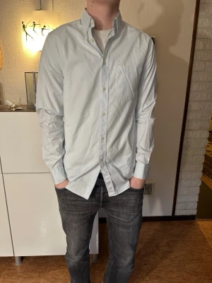 Ljusblå skjorta från J.Lindberg - Snygg ljusblå skjorta med klassisk krage och knäppning framtill. Skjortan har lång ärm och bröstficka, perfekt för en clean och stilren look. Tillverkad i bomull för en skön känsla. Är S i storleken men passar även M. Märke J.Lindberg