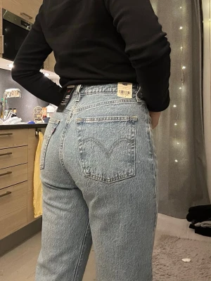Levi's ljusblå ribcage straight - Säljer ett par ljusblå raka jeans från Levi's med hög midja och klassiska bakfickor. Jeansen har en vintageinspirerad tvätt och är tillverkade i ett robust denimtyg. Perfekta för en avslappnad och trendig look. Säljer för att den är för liten för mig. W26 L30