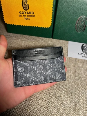 Svart plånbok kortfodral från Goy4ard - Snyggt svart plånbok kortfodral från Goy4ard med klassiskt mönster i vitt och grått. Tillverkat i canvas och läder med flera fack för kort. Perfekt för dig som vill ha en stilren och exklusiv accessoar i fickan.