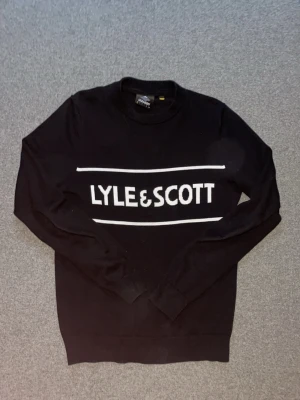 Svart sweatshirt från Lyle & Scott - Säljer en svart sweatshirt från Lyle & Scott med vit logga och linjer framtill. Tröjan har rund halsringning, långa ärmar och ribbade muddar vid ärmslut och nederkant. Perfekt för en clean och stilren look. Xs passar mig som är S 