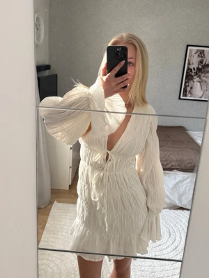 Strukturerad miniklänning med knytdetalj - Jättefin och helt slutsåld vit klänning från Moa Mattsons kollektion med NA-KD. Helt oanvänd med prislappen kvar. Passar perfekt nu till studenten och sommaren🥰  Säljer då den tyvärr inte kommer till användning. Hör gärna av dig vid frågor 🤍
