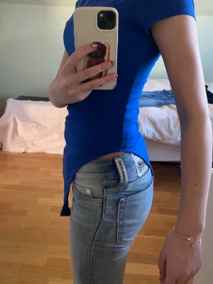 Kornblå tight body - Snygg kornblå t-shirts body med tight passform och korta ärmar. Bodyn har en klassisk rund halsringning och är tillverkad i ett stretchigt material som sitter skönt mot kroppen. Perfekt för en stilren och enkel look.