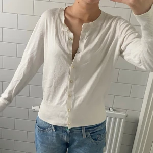 Vit kofta med guldiga knappar - Söt finstickad vit kofta med guldknappar från Holly & Whyte/Lindex. Endast använd ett fåtal gånger så väldigt fint skick! Jätte fin att slänga över nu till våren och sommaren 😊🌸