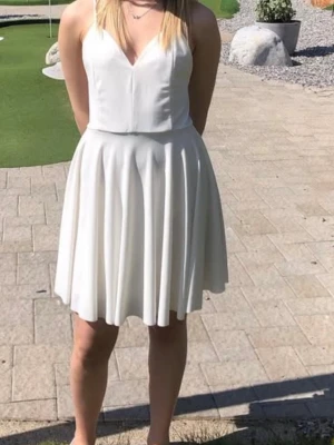 Vit kort klänning med smala axelband - Säljer en vit kort klänning med smala axelband och v-ringad urringning från bikbok i storlek XS. Klänningen har en utsvängd kjol, passar perfekt som examensklänning💞 