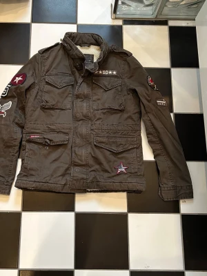 Superdry jacka  - Säljer en stilren jacka från Superdry i snygg mörkgrön färg. Märkt storlek S, men är liten i storleken och passar bättre som XS.  Jackan är i fint skick och perfekt för både vardag och höst/vår.   ✅ Storlek: S (liten – motsvarar XS) ✅ Färg: Mörkgrön ✅ Skick: mycket bra   Hör av dig vid intresse eller för fler bilder 