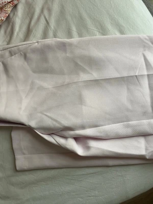 Ljusrosa kostymbyxor - Säljer ett par ljusrosa kostymbyxor med raka ben och klassisk passform. Byxorna har hällor för skärp och sidfickor. Materialet känns mjukt och har en lätt struktur, perfekt för en clean och stilren look.l low waist 