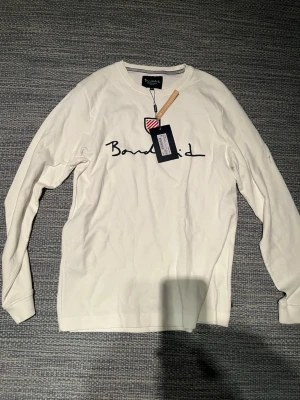 Vit långärmad tröja från Bondelid - Vit långärmad tröja från Bondelid med svart logotyp på bröstet. Tröjan är tillverkad av bomull och har en klassisk rund halsringning. Perfekt för en avslappnad och stilren look. Är helt ny och aldrig använd säljer pga storlek 