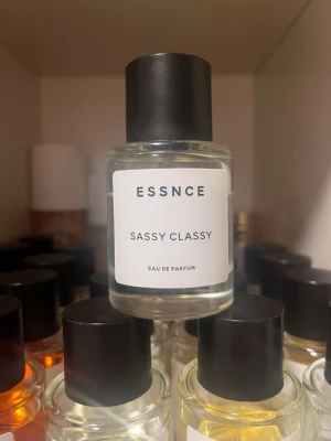 ESSNCE Sassy Classy Eau de Parfum - ESSNCE Sassy Classy Eau de Parfum kommer i en stilren, rund glasflaska med svart lock och vit etikett. Doften är elegant och modern, perfekt för dig som gillar en fräsch och självsäker parfym. Flaskan har minimalistisk design och transparent vätska.