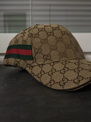 Gucci beige keps med GG-mönster - Säljer en beige keps med det klassiska GG-monogrammet över hela kepsen. Skriv för mer information om varan den är helt ny och storleken justerbar .
