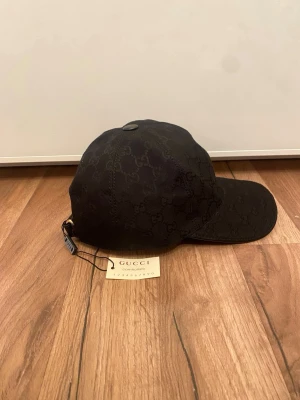 Gucci keps  - Snygg svart keps från Gucci med det klassiska GG-monogrammet över hela kepsen. Justerbar rem bak med metallspänne och diskret etikett. Tillverkad i ett slitstarkt tyg som ger en exklusiv känsla. Perfekt accessoar för en trendig och lyxig look.