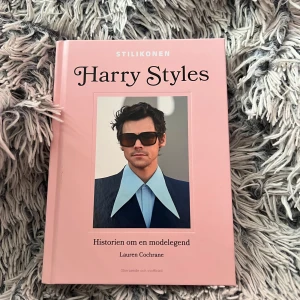 Harry Styles - Historien om en modelegend - Säljer boken 'Harry Styles - Historien om en modelegend' av Lauren Cochrane. Boken har ett rosa hårt omslag med porträtt på framsidan och stilfull design. Perfekt för dig som vill läsa om Harry Styles och hans ikoniska mode och personlighet.