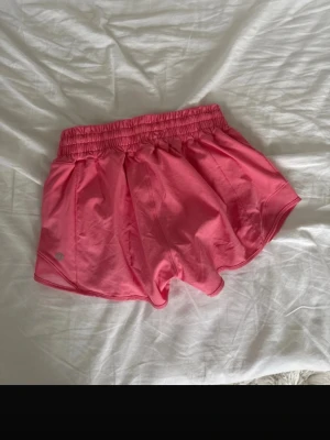 Rosa träningsshorts från lululemon - Snygga rosa träningsshorts från lululemon med elastisk midja och sportig design. Shortsen har en loose passform och är tillverkade i ett lätt och snabbtorkande material, perfekta för aktiva dagar. Klassisk modell med diskret logga på sidan. SÅÅÅÅÅ SNYGGGAAA 💓💓🫰🏼🫰🏼🫰🏼🥹🥹 (bilderna är från min vinted violasavolainen)!!