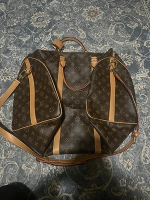 Louis Vuitton Monogram resväska - Snygg resväska från Louis Vuitton i klassiskt brunt monogrammönster med beigea detaljer och axelrem i läder. Väskan har två stora ytterfickor, handtag och avtagbar adressbricka. Perfekt för dig som vill resa med stil och ha plats för allt du behöver.