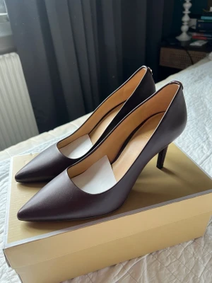 Bruna pumps från Michael Kors - Snygga pumps från Michael Kors med spetsig tå och klassisk design. Skorna har en elegant klack och är tillverkade i slätt läder med beige innersula. Perfekta för dig som vill ha en stilren och tidlös look. Superfina, oanvända eleganta klackar i skinn och i höstens heta färg. Storlek 38 men är som en 37 och tyvärr för små för mig. Hoppas på ett nytt hem till dem!  Nypris : 1399kr - mitt pris 700kr  Finns i Sköndal alt Skanstull.
