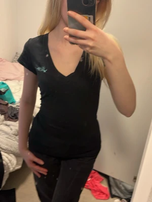 Svart v-ringad t-shirt från peak performance  - Säljer en svart t-shirt från Odd Molly med v-ringning och korta ärmar. Liten ljusblå broderad logga på bröstet. T-shirten har en figurnära passform och är gjord i mjuk bomull, perfekt till jeans eller kjol.