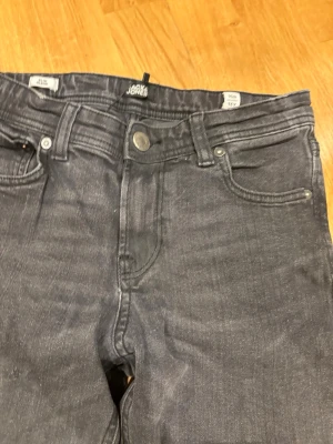 Mörkgrå jeans från Jack & Jones - Snygga mörkgrå jeans från Jack & Jones med klassisk femficksmodell och raka ben. Jeansen har normal midja och är tillverkade i ett mjukt denimtyg med lite stretch för extra komfort. Perfekta för en avslappnad och trendig look.lite mer lose fit 