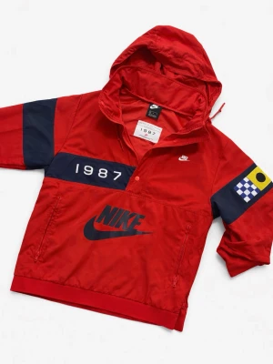 Nike M NSW Reissue Walliwaw Woven Jacket.  - Sällsynt vindjacka från Nike med stor logga framtill, trycket '1987' på bröstet och marinblå detaljer på ärmarna. Jackan har huva med dragsko, halv knappslå och dragkedjor på fickorna. Materialet är troligtvis polyester och jackan har en sportig look med färgglad patch på ena ärmen. Jackan säljs inte ny länge. 
