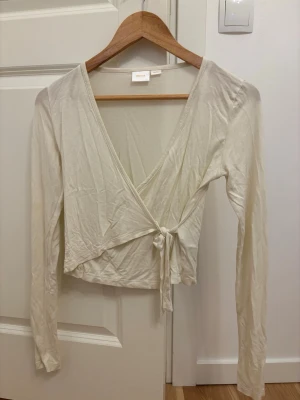 Krämvit tröja med knyt - Snygg vit omlottopp från Ginatricot med långa ärmar och knyt i sidan. Den är i storlek 158/164 men passar perfekt som XS. Toppen har tyvärr 2 sådana små hål som visas på bilden. 