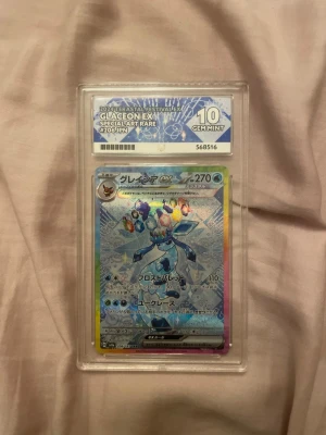 Pokémon Glaceon EX Special Art Rare - Japanskt Pokémonkort Glaceon EX Special Art Rare #206 från Astral Festival, graderat 10 GEM MINT av ACE Grading. Kortet har en holografisk yta med blå och regnbågsfärgade detaljer och är inkapslat i ett genomskinligt plastfodral.