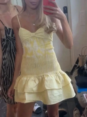 Gul kort klänning med volang - Söt gul kort klänning med smala axelband och volang nertill. Klänningen har en lätt rynkad överdel och är perfekt för varma dagar. Den har en feminin och somrig look med en figurnära passform upptill och utställd kjol.