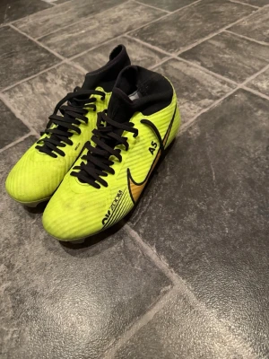 Nike Air Zoom fotbollsskor gul/svart - Säljer ett par Nike Air Zoom fotbollsskor i en riktigt snygg gul färg med svarta detaljer och guldigt swoosh. Skorna har snörning och en högre strumpliknande krage för extra stöd. Perfekta för dig som vill sticka ut på planen! Coustom skor med AS text 